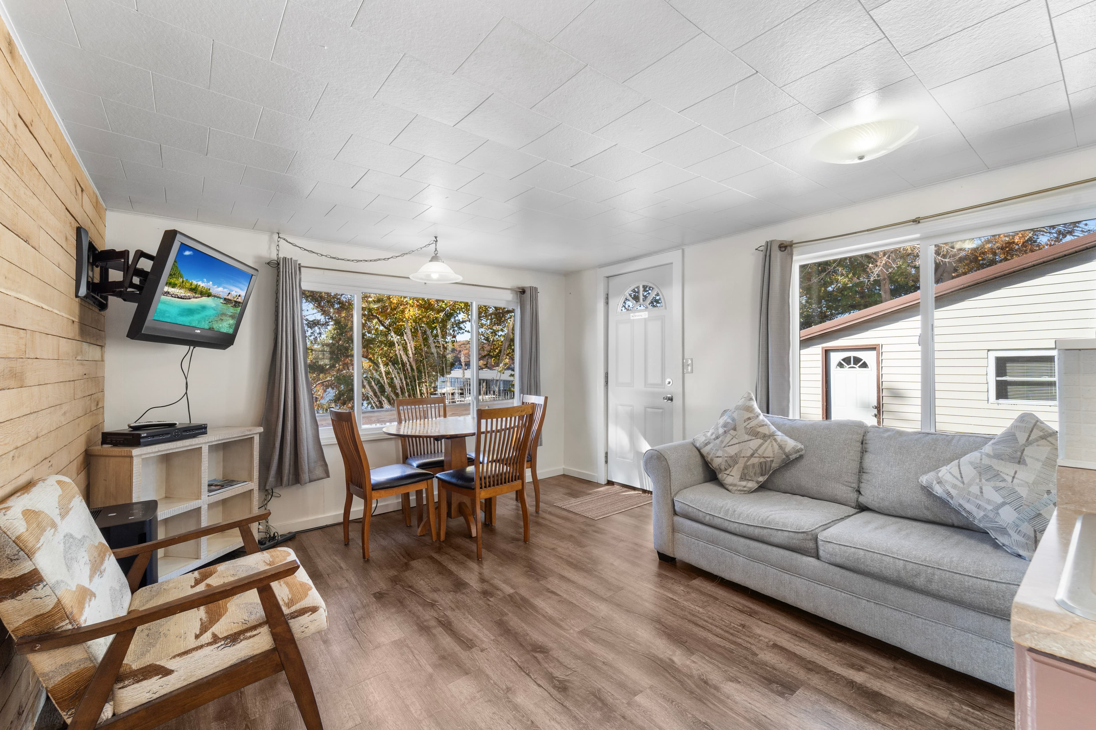 Cozy living space featuring a sofa, dining table, TV, and large windows with natural light.