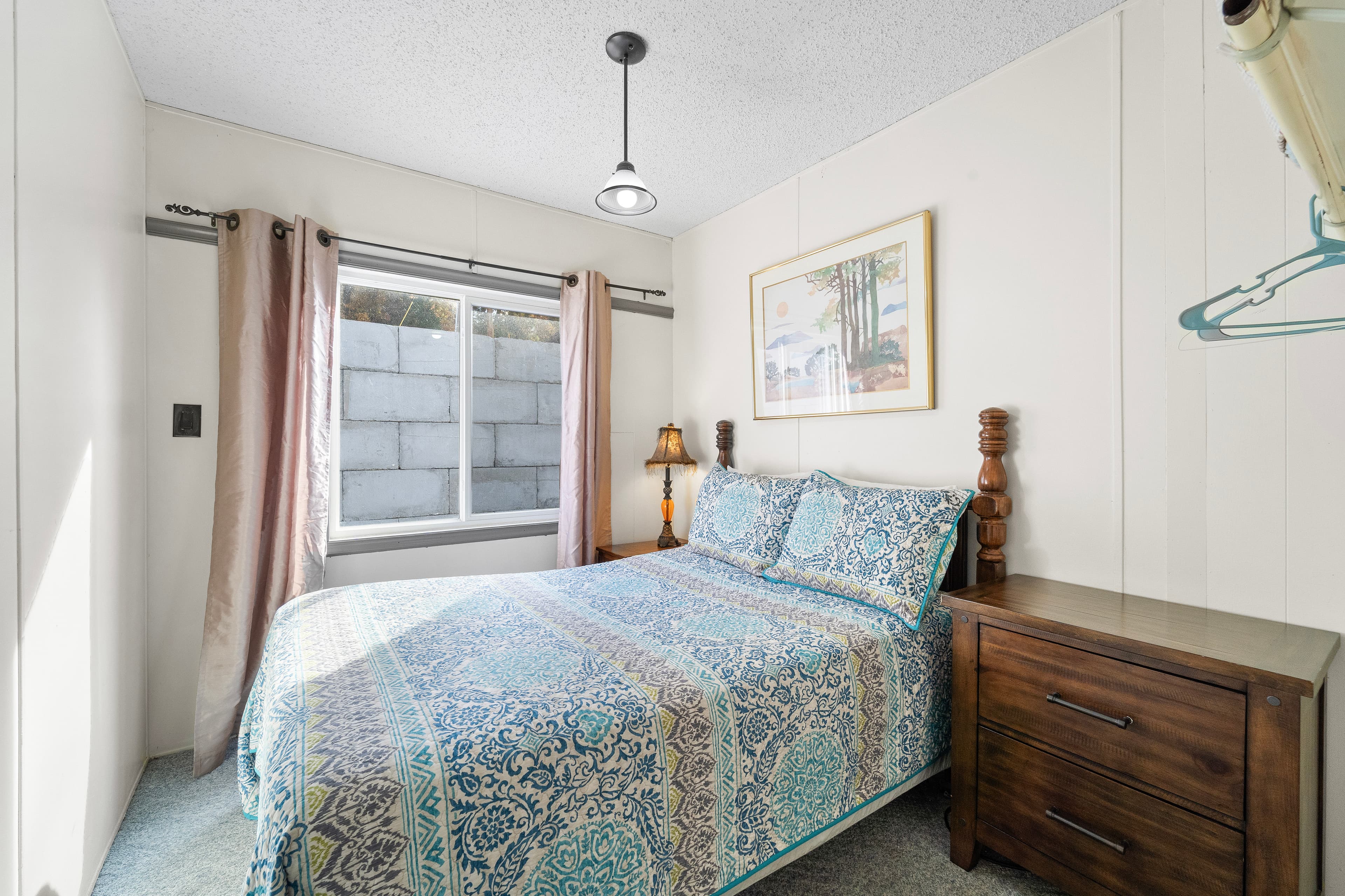 A cozy bedroom featuring a bed with a patterned comforter, a wooden nightstand, and a window with curtains.