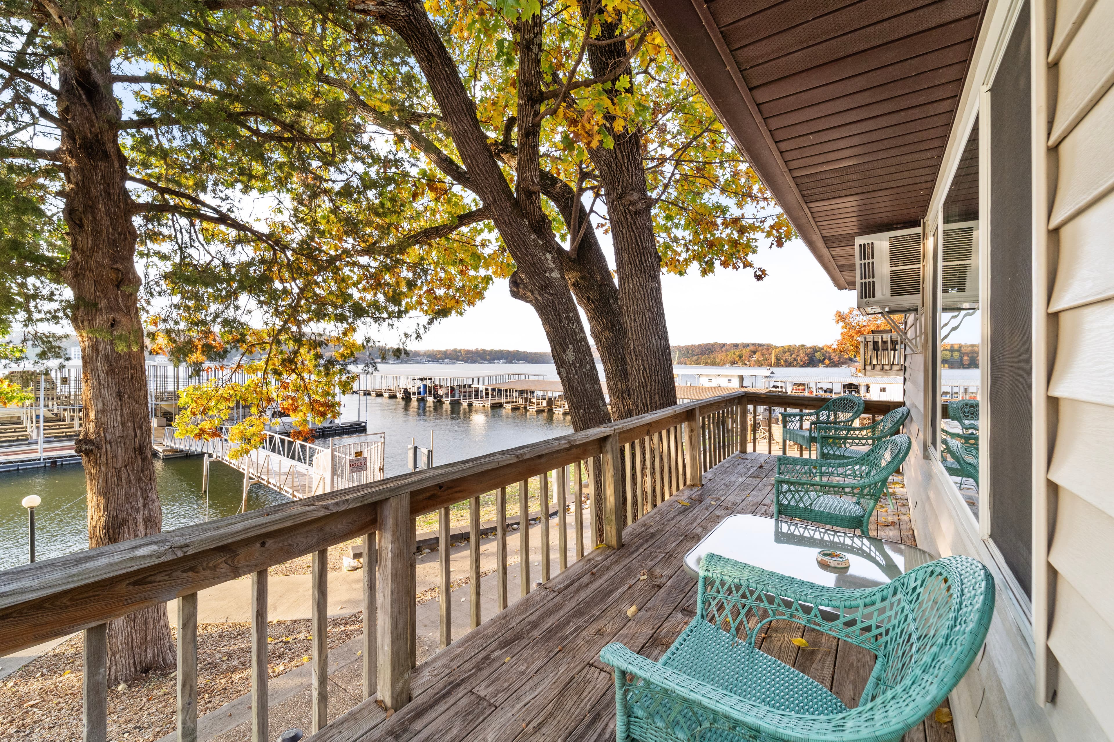 A cozy deck with teal chairs overlooks a tranquil marina surrounded by autumn foliage.