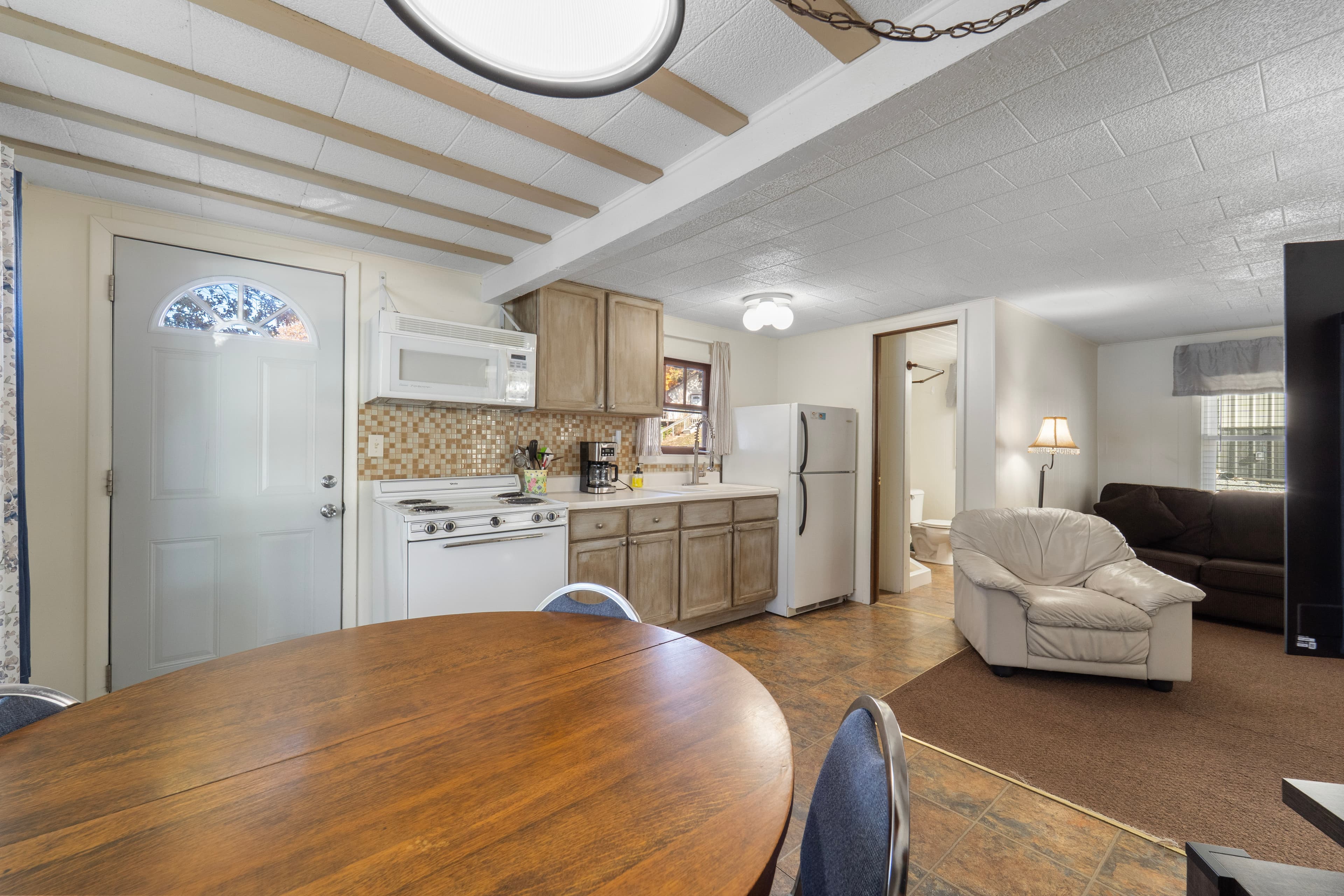 A cozy kitchen and dining area featuring a round wooden table, light wood cabinets, and a living room with a beige couch.