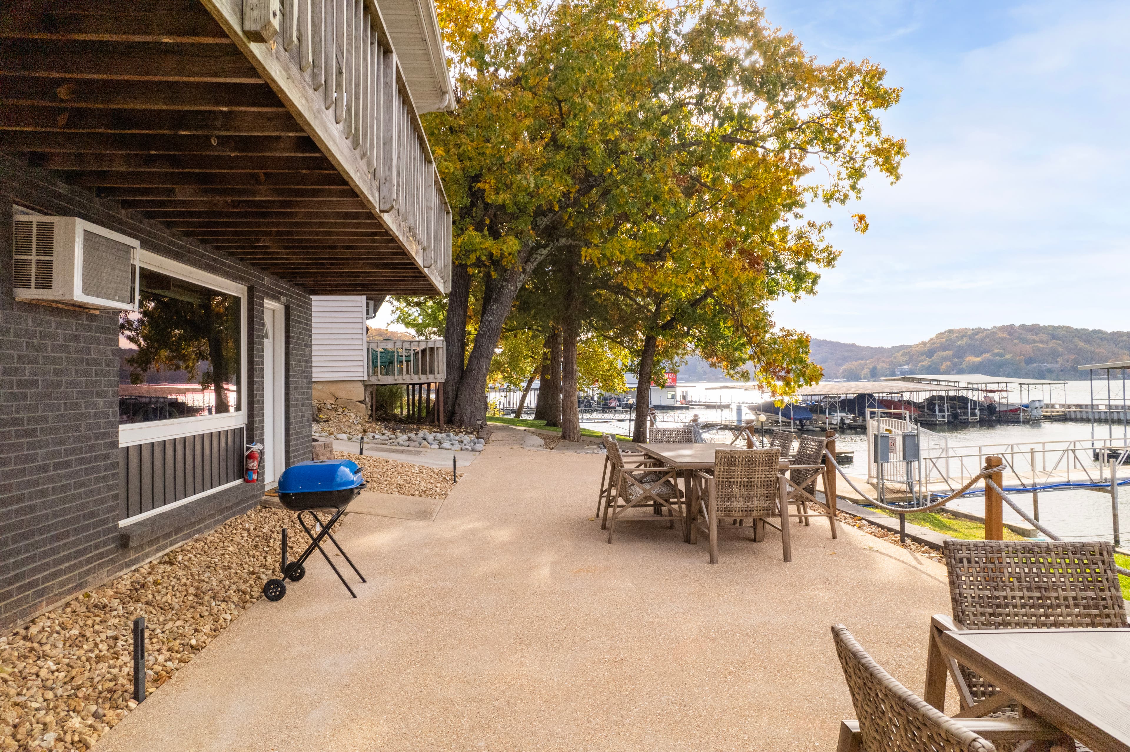 A patio area with a grill, seating, and a view of a lake and nearby docks.