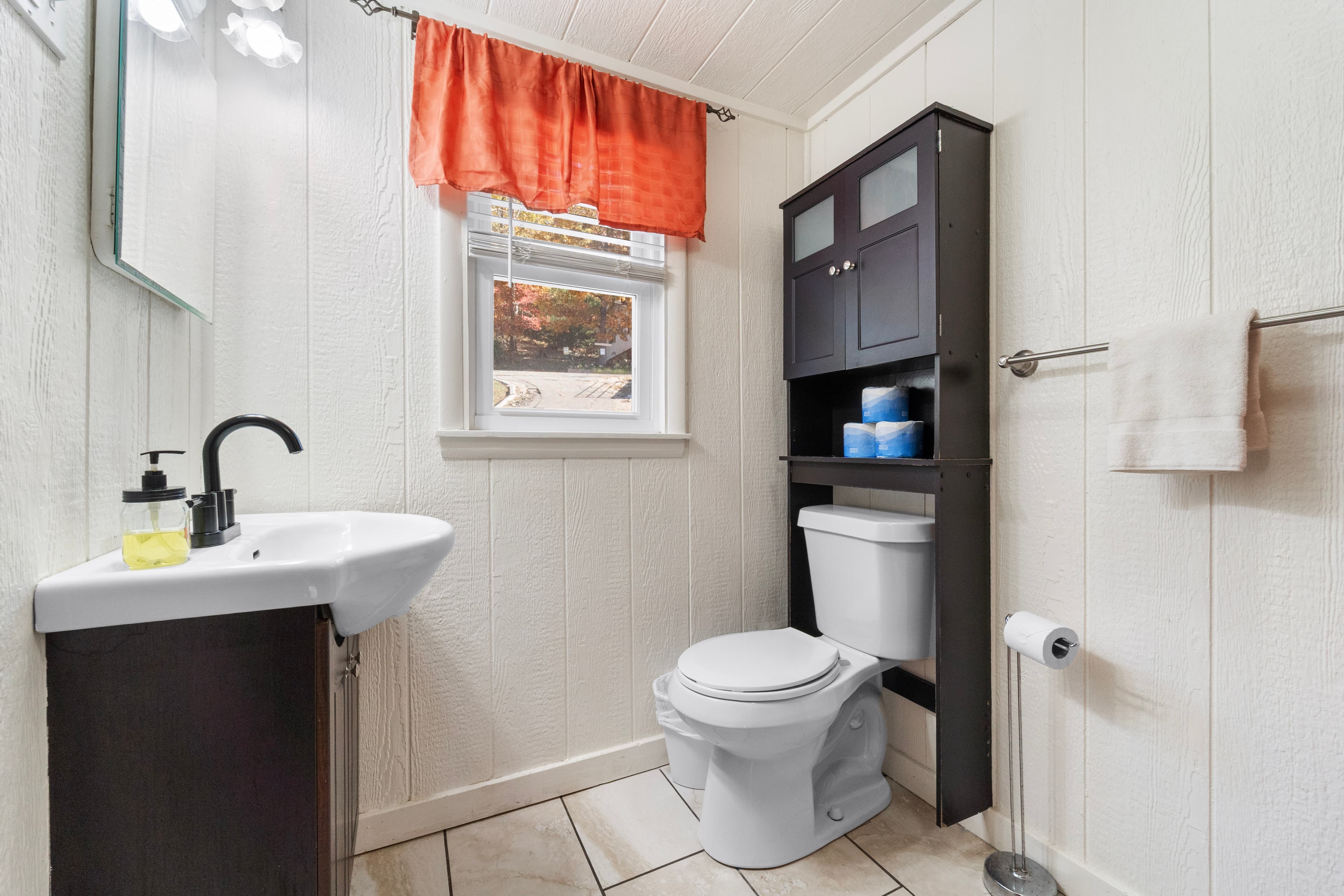 A clean and modern bathroom featuring a sink, toilet, and dark wood shelving unit with blue towels.