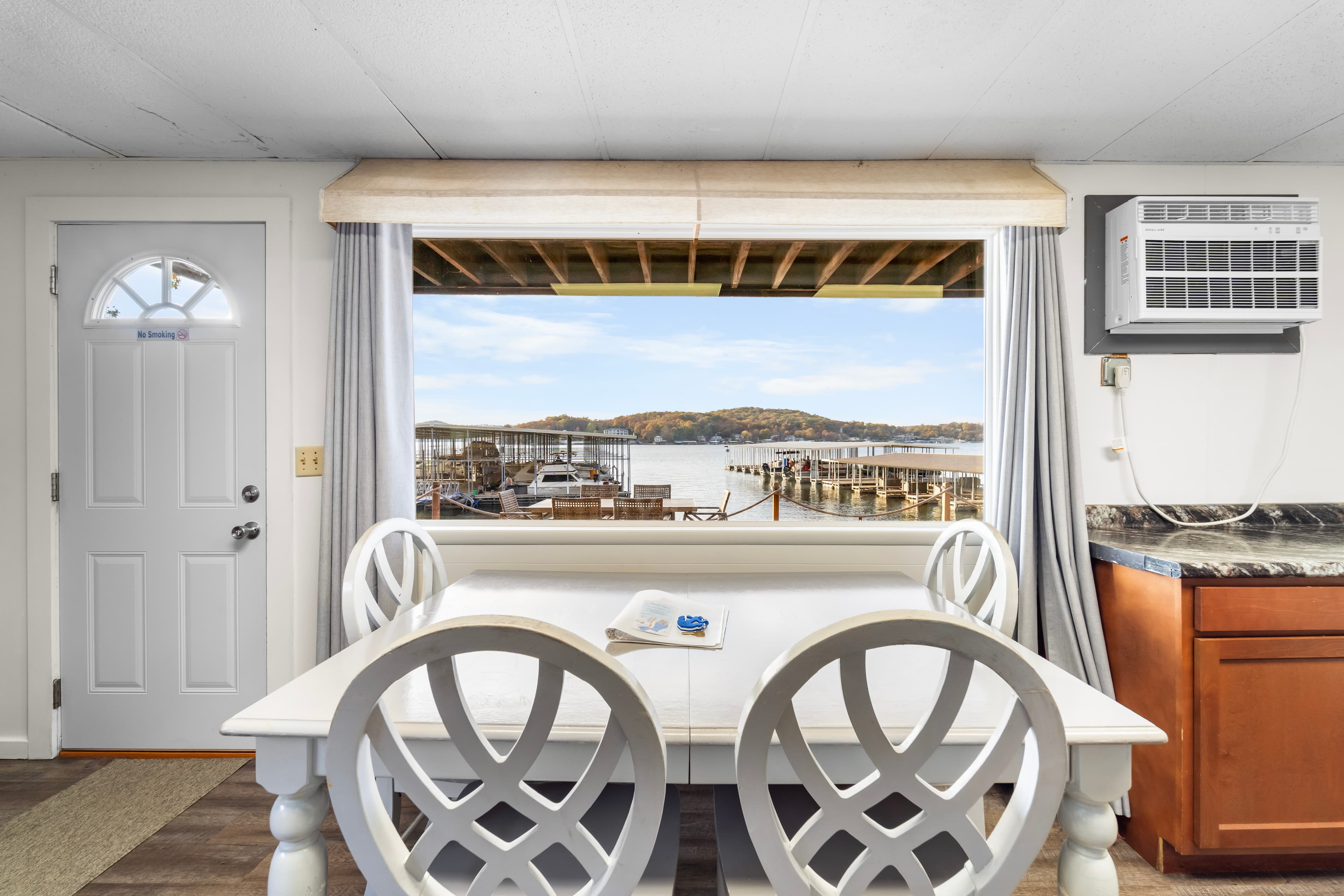 Dining area with two white chairs, overlooking a lakeside view through a large window.